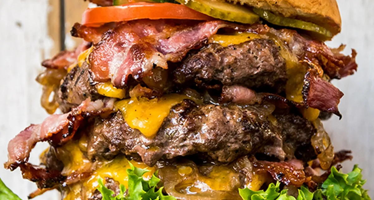 Nahaufnahme eines mehrlagigen Burgers mit Kaese und Salat